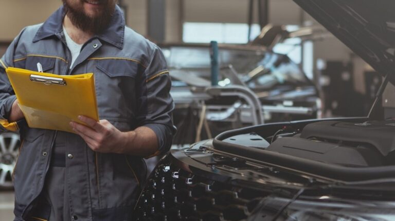 Car mechanic with clip board looking at car engine