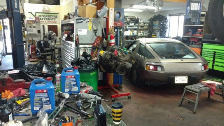 Inside a classic car restoration shop[ with tools and parts with a silver Porsche