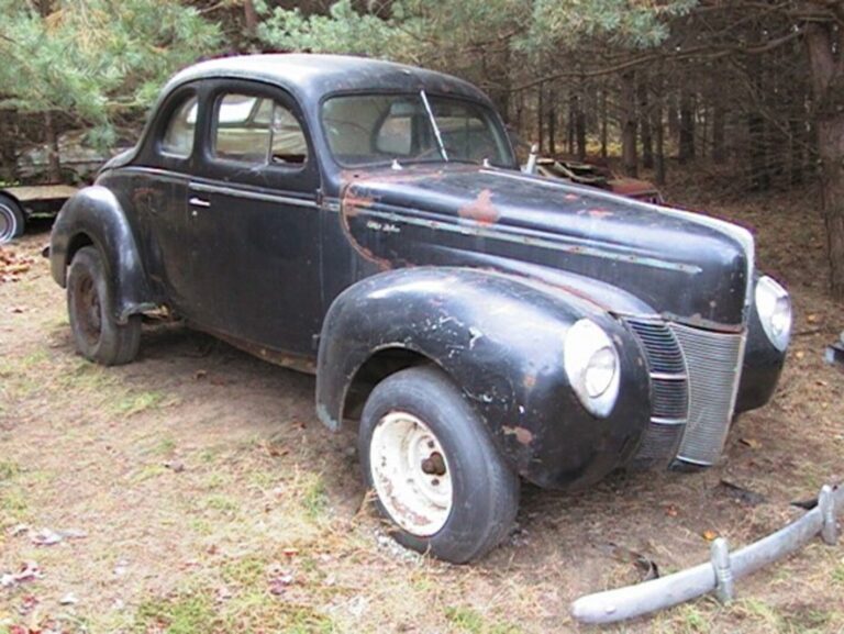 Black 1940 Ford Coupe sitting in a yard under pine trees