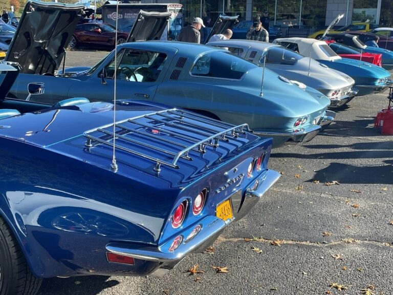 A line of 3 blue and 1 silver 1960s Corvettes from the rear angle