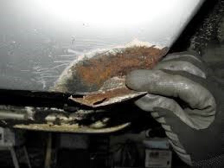 A rusting panel on a silver car fender being held by a hand