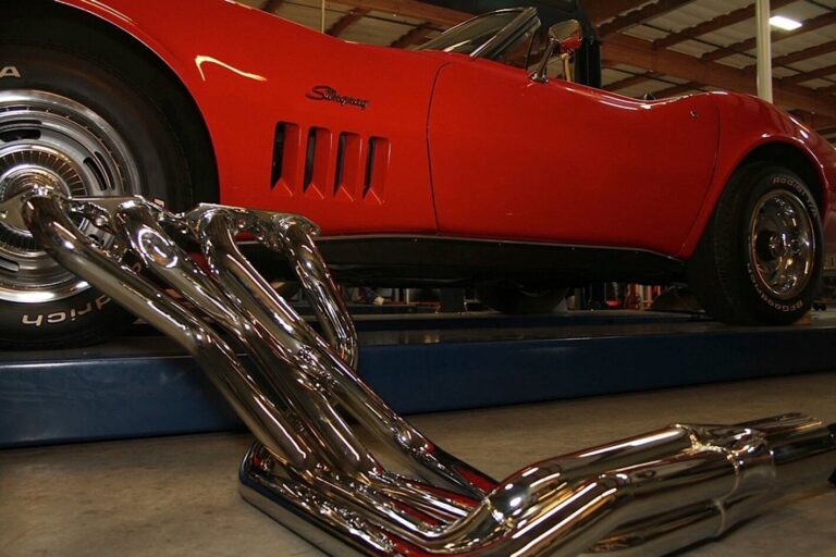 Chrome car headers leaning against a red Corvette