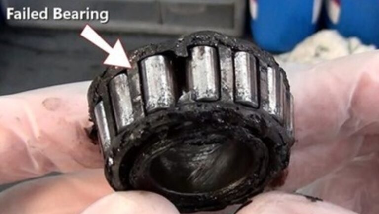 A person holding a rear differential axel bearing with damage noted by white arrow