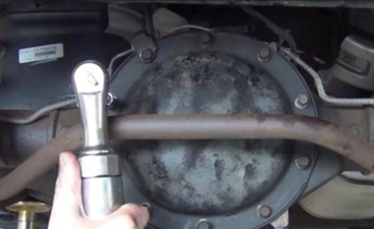 A person installing the bolts thru the cover onto the rear differential using an air ratchet