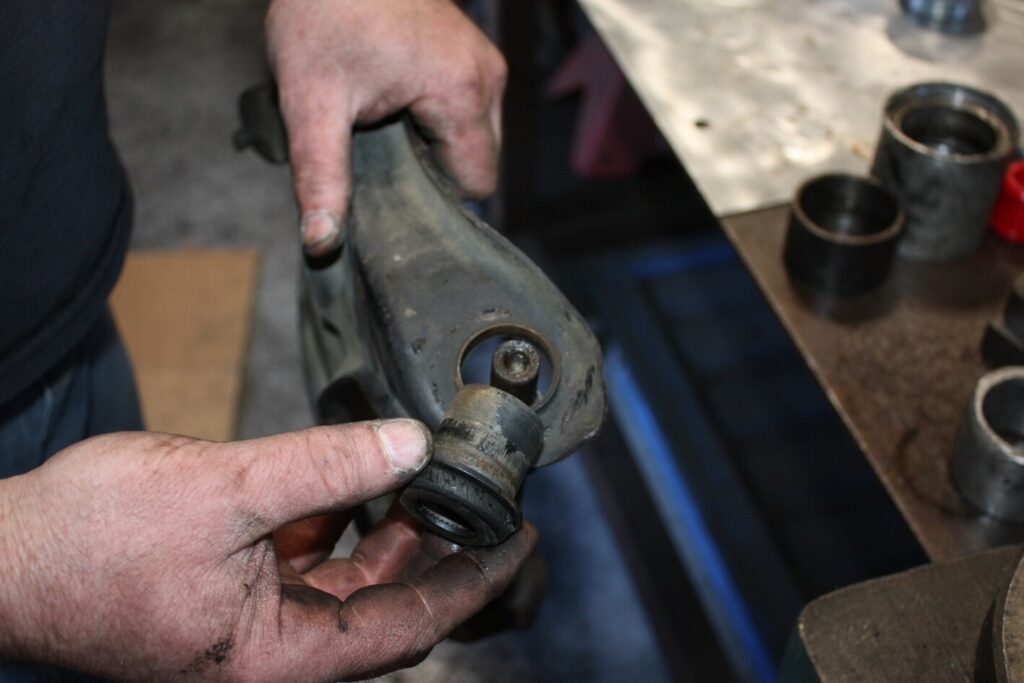 A person holding a control arm with suspension bushings