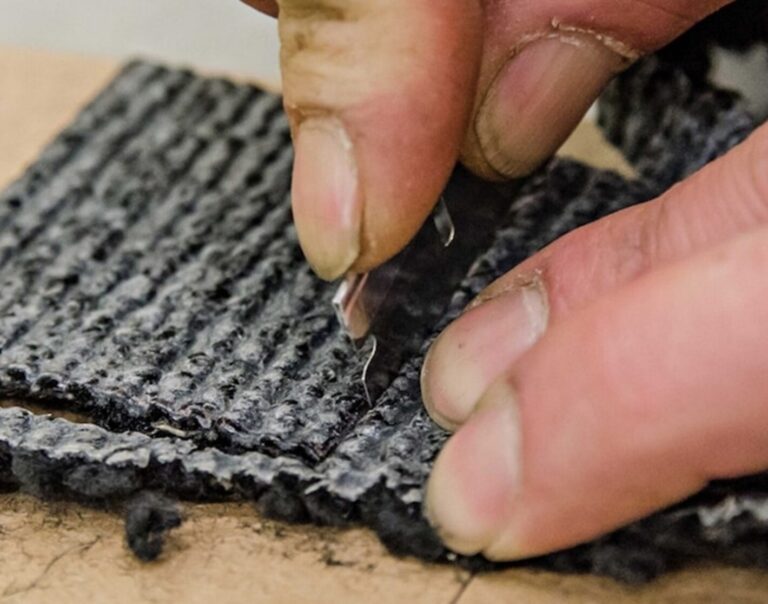 A person trimming car carpet with a razor blade
