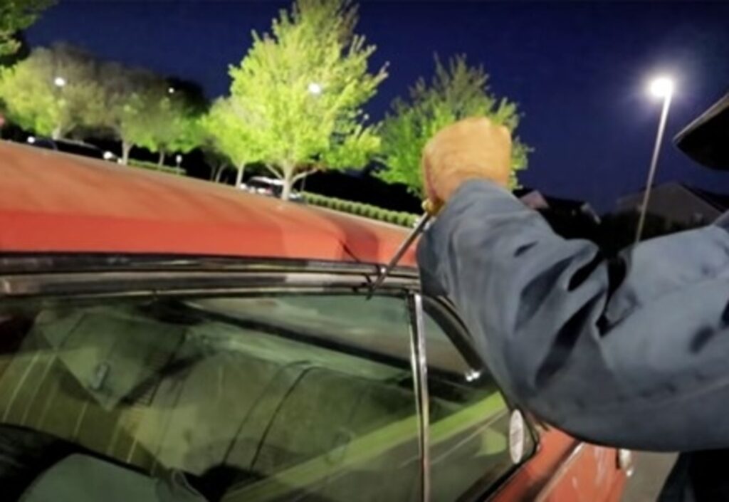 A man trying to break into an orange classic car thru the window