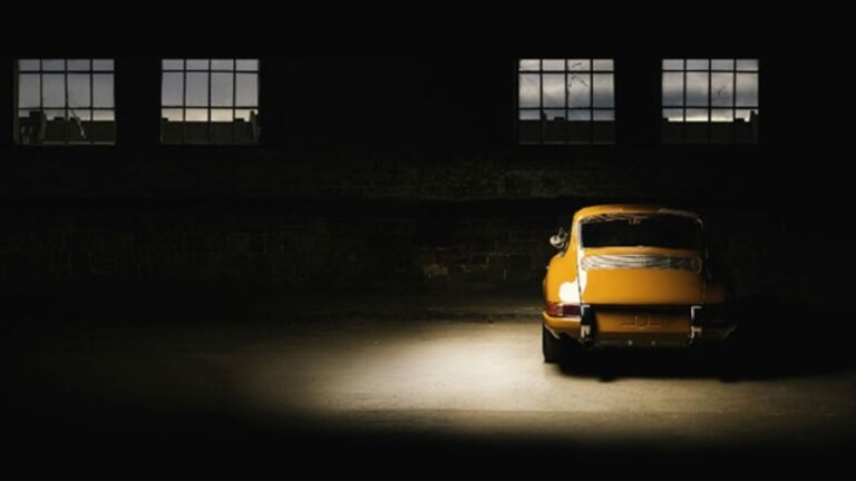 A yellow Porsche inside a dark garage wit ha single light over it