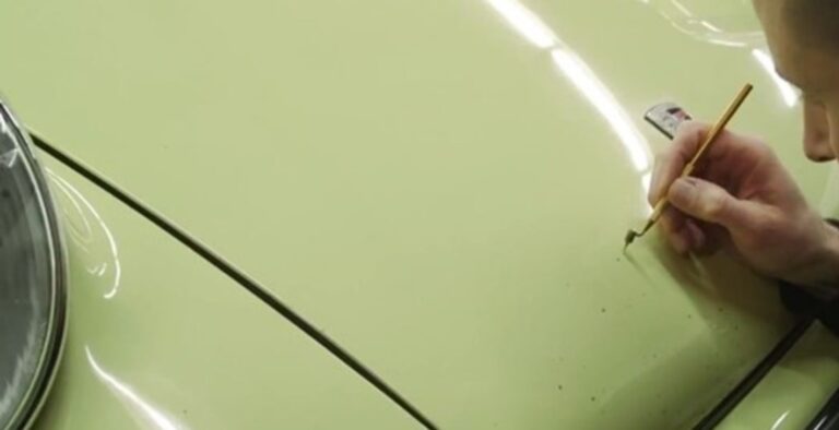 A man touching up paint scratches on the hood of a yellow Porsche