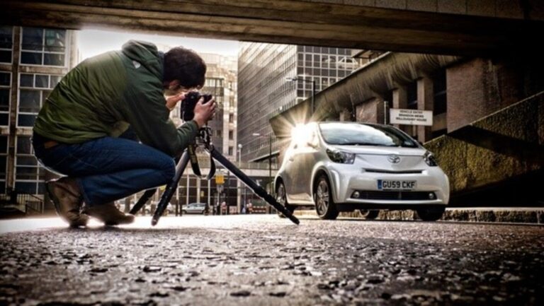 A man taking a picture of a white car using a camera on a tri-pod