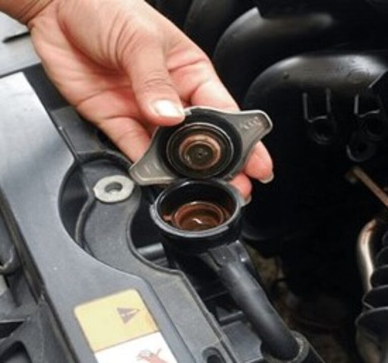 A person holding a radiator cap over the radiator fill on a car