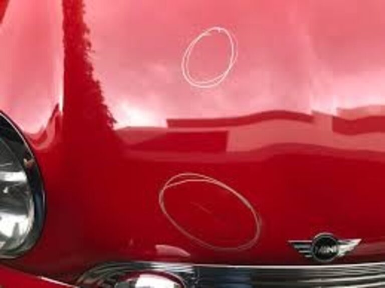 Rock chip damage to a red Mini Cooper front hood prior to paint touch-up