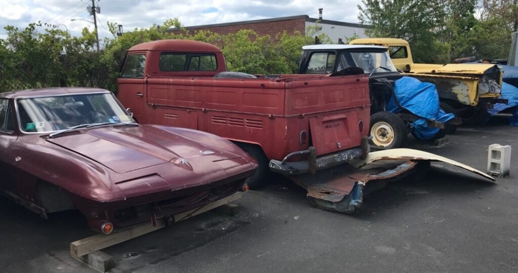 Corvette, VW van, and 2 pickup trucks disassembled and parked at a restoration shop