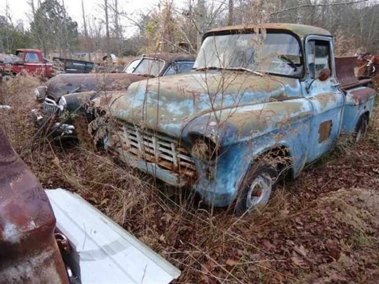 A 50s blue Chevy truck and black sedan in a field which you may see when finding junkyard parts