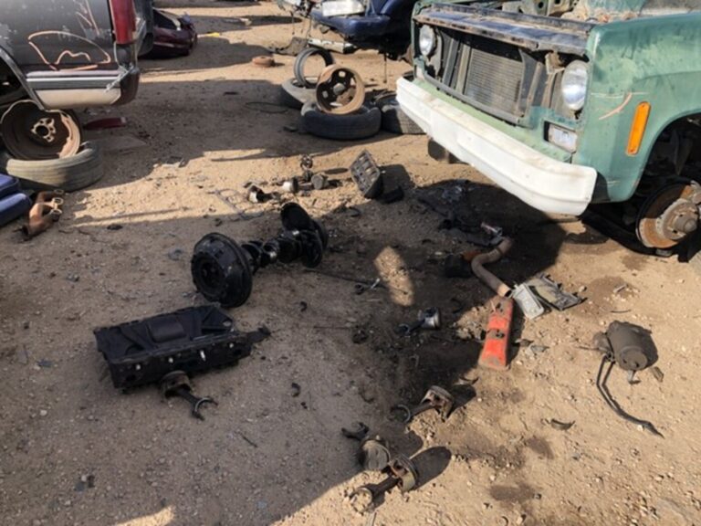 Truck parts taken out a junked green truck laying on the ground at front of the truck after finding junkyard parts