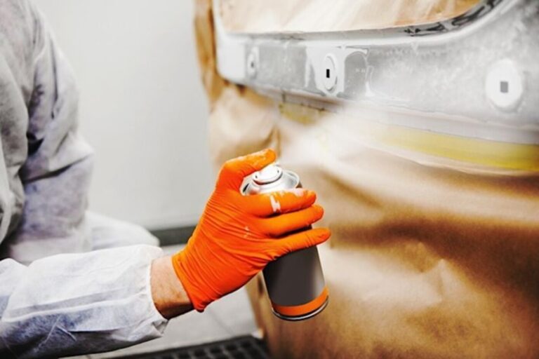 A person wearing orange rubber gloves to spray white car paint using a spray can