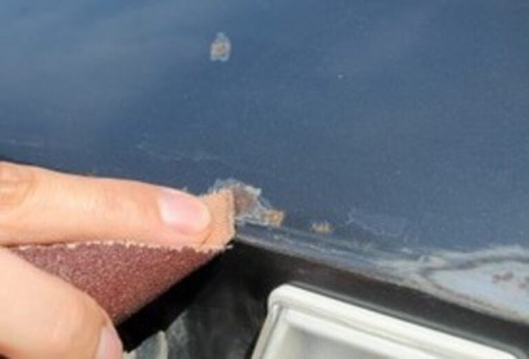 A person sanding down a rusted area on a blue car as part of rust repair