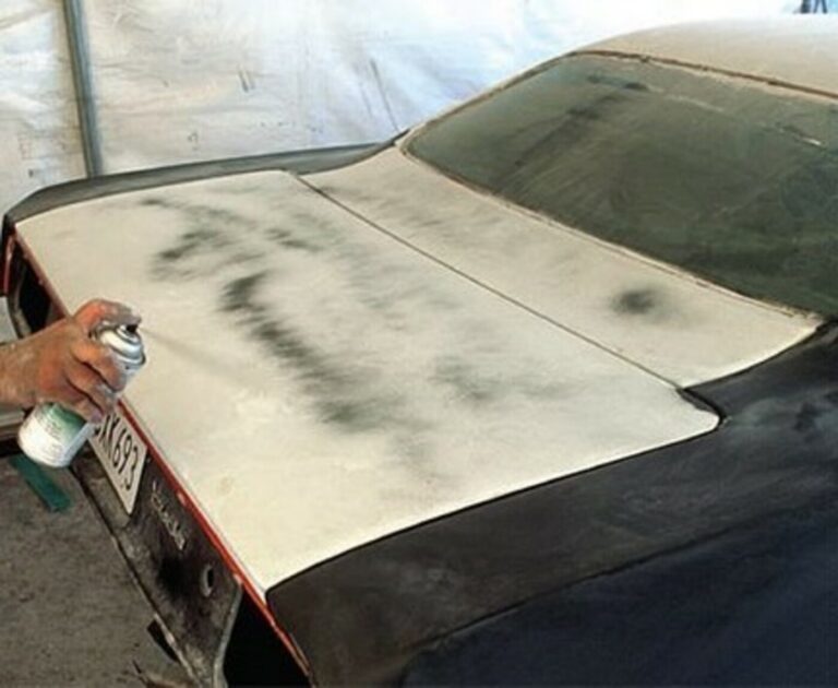 A person spraying primer on the rear trunk lid of a Plymouth Cuda in white