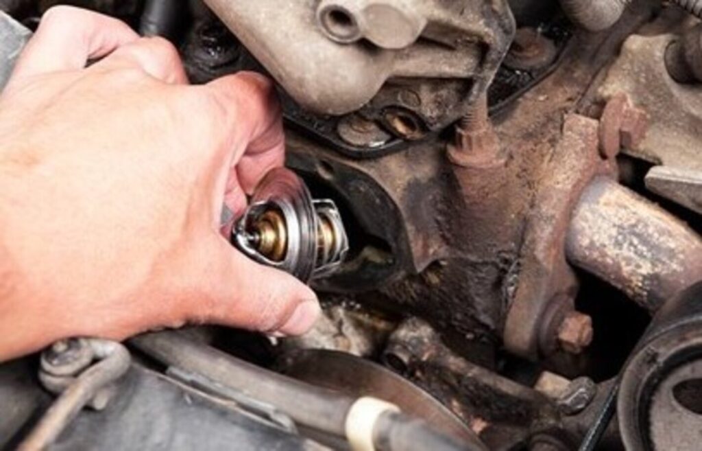 A mechanic installing a new thermostat into its housing on an old car engine