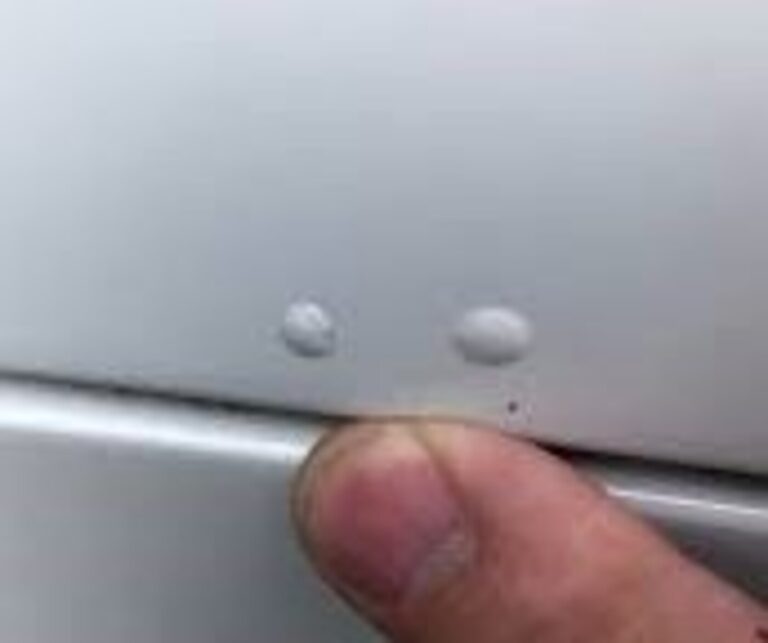 A person pointing 2 tiny bubbles under silver car paint