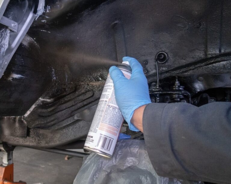 A mechanic applying rubberized rustproofing in a wheel well of a white car
