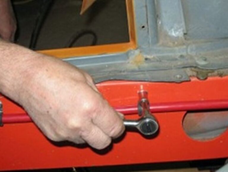 A mechanic installing the red positive lead from the front to the rear of the car on the side of a red frame rail for battery relocation