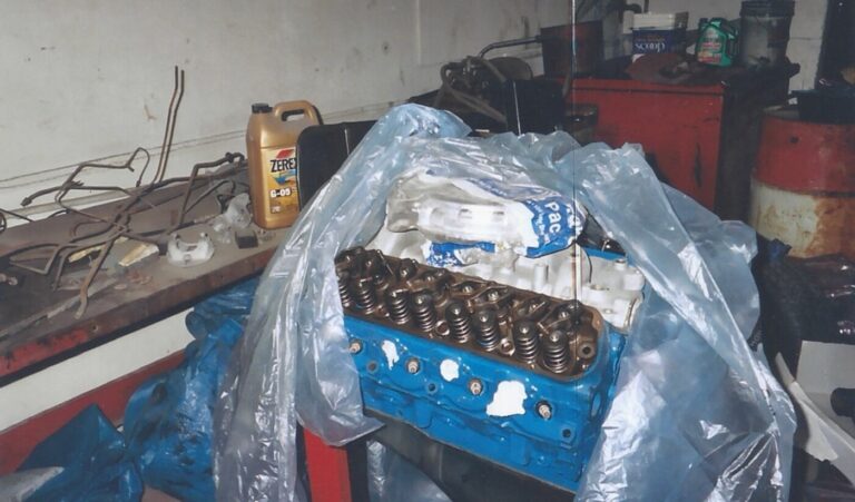 A blue painted Ford 302 engine in a palstic wrapper on an engine stand in a workshop after being returned from engine rebuilding