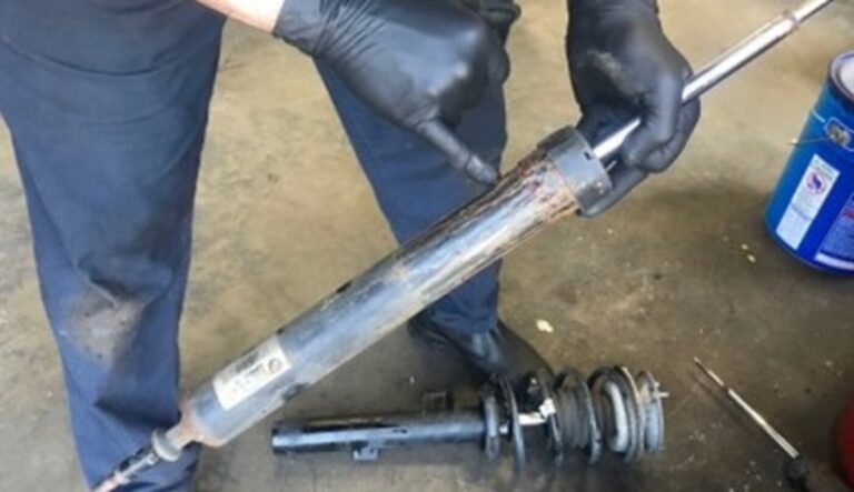 A mechanic pointing with a finger where fluid is leaking from the top of a worn black shock absorber