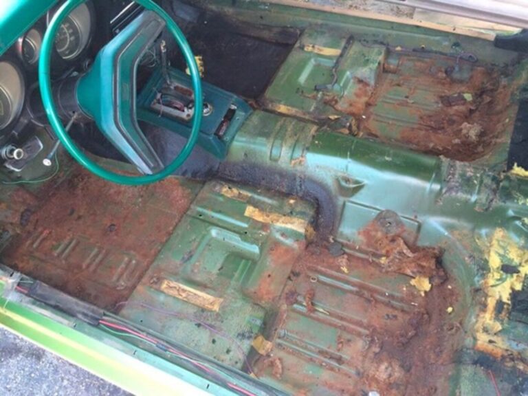 The interior of a green cord with a floor shifter with the car's interior carpet removed showing the rusty floor