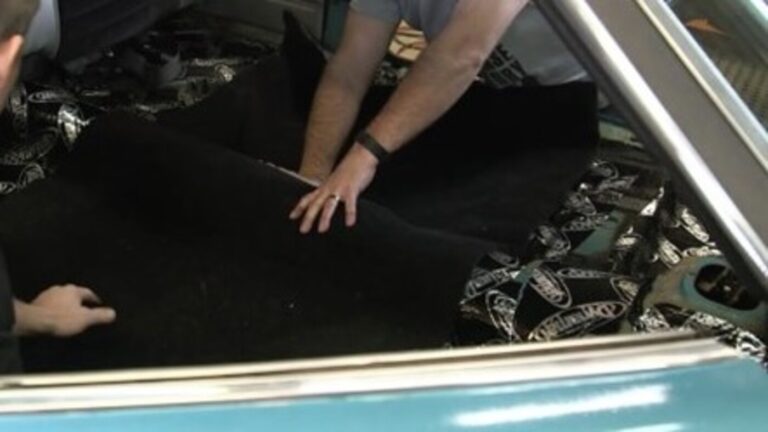 2 men installing a new black car interior carpet kit into a blue car