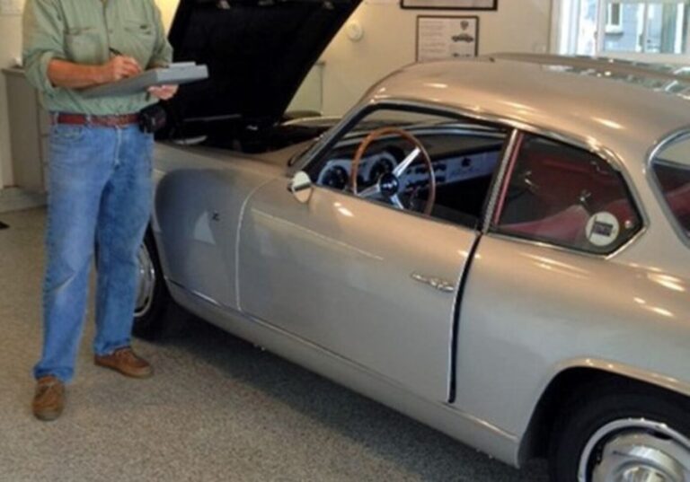 A classic car inspector in blue jeans and green shirt inspecting a silver vintage car to help avoid counterfeiter scams