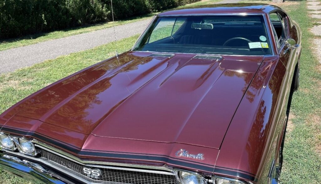 Looking down on the hood of a maroon 68 Chevy Chevelle sitting on a grass lawn and car polishing and waxing