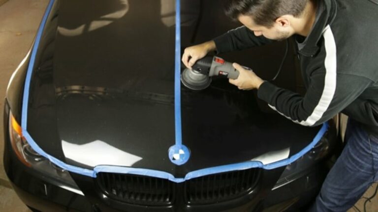 A detailer with a poloiishing wheel working on the hood of a black BMW with blue tape separating the area not being polished vs the area he is car polishing