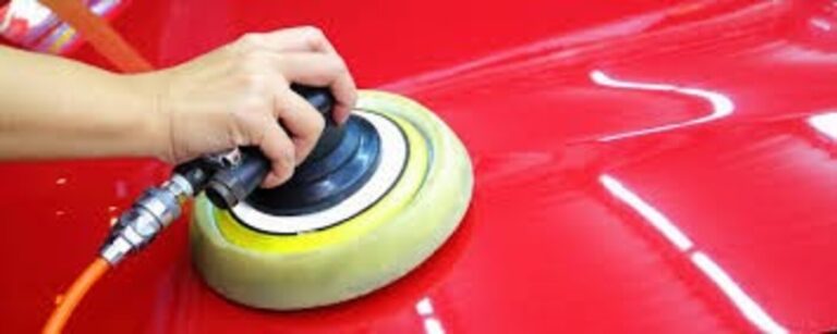A detailer working wit ha polishing wheel on a red car hood while car polishing
