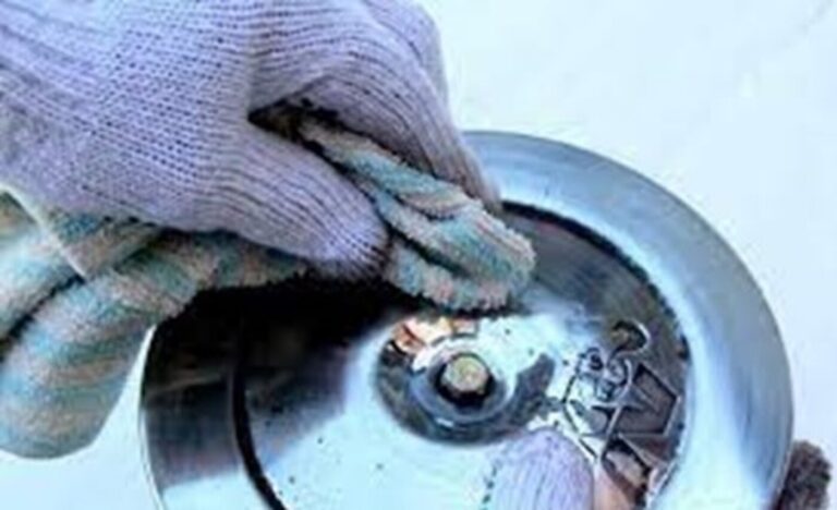 A person with a blue wool glove and rag polished a chrome air cleaner cover in car show display preparation