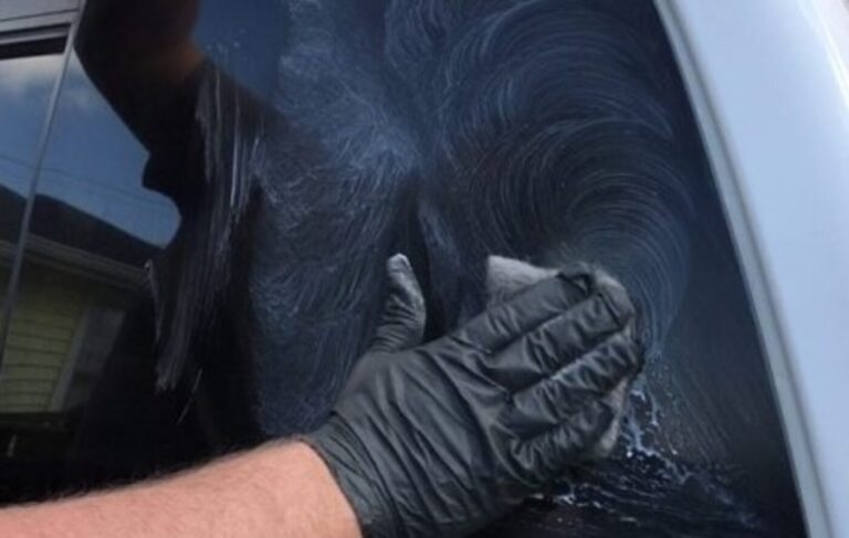A person with black rubber glove wiping cleaning past on car window to remove water spots
