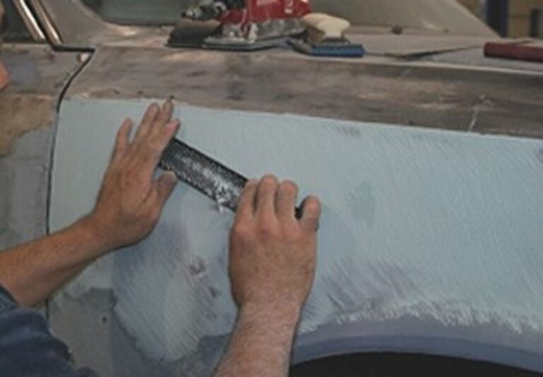 A mechanic sanding down body filler with a "cheese grader" on a car fender as part of the autobody repair