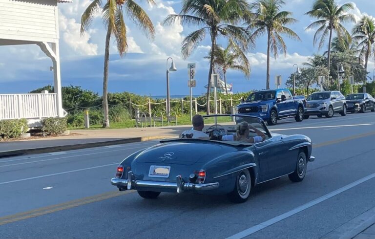 A classic blue Mercedes 190 SL driving along A1A in Florida with palm trees and the Atlantic Ocean in the background for waterside road trips