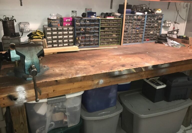 A work bench with vise and hardware in containers with plastic storage bins underneath setting up before starting a car restoration