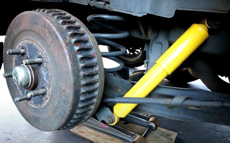 A yellow shock absorber installed on the rear suspension components attaching the lower control arm to the car frame