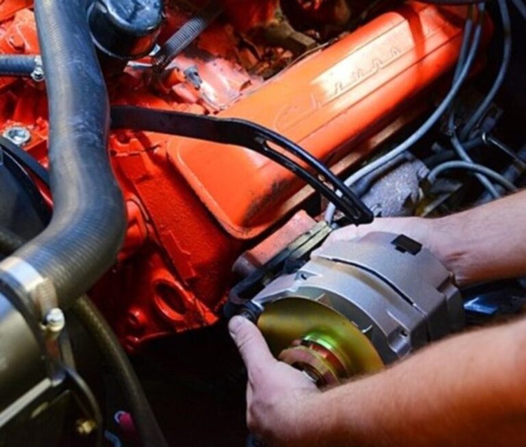 A mechanic installing a new alternator on an orange Chevrolet engine
