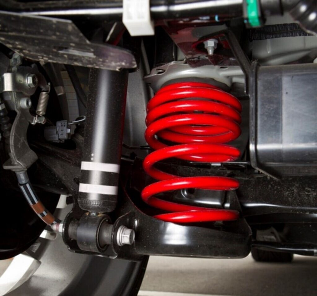 A red rear coil spring installed on a car next to a black shock absorber on the rear axel