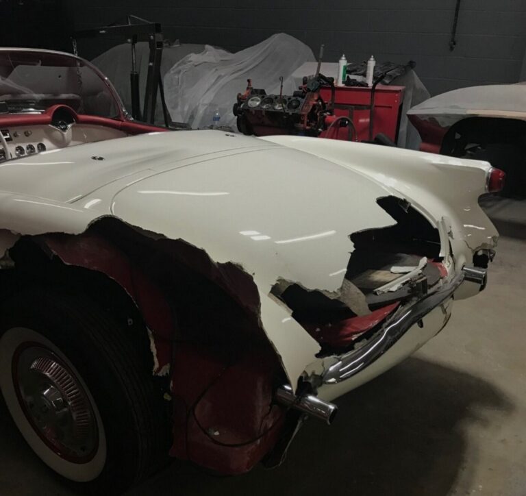 A white 1953 Chevy Corvette with the rear end of the car fiberglass damaged with holes after car shipping in the car repair shop
