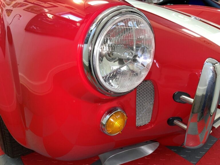 The passenger side front of a red Cobra sowing its headlight, turn signal, bumper and air vent