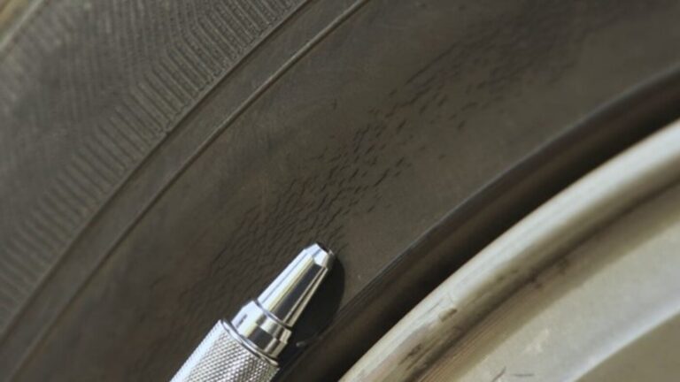 A silver pen being used to point to car tire dry rot on the sidewall of the black tire