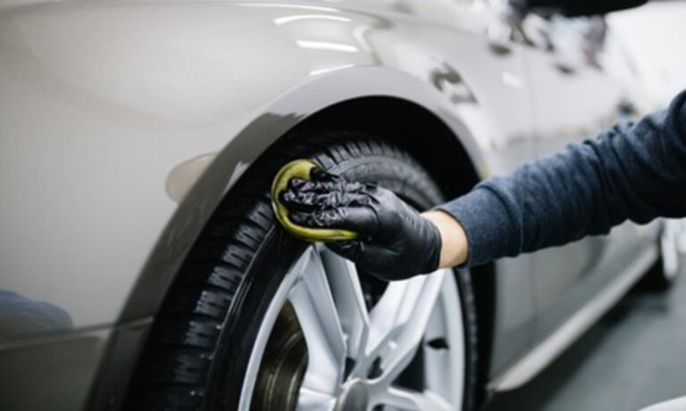 A mechanic spreading a protective chemical onto a car tire with an applicator to prevent car tire dry rot