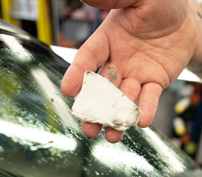 A detailer with white clay-bar in his hand showing the dirt cleaned from a windshield for spot car glass cleaning