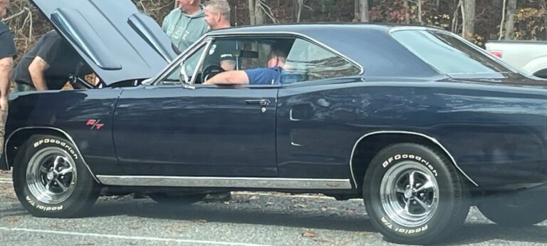 A blue Plymouth Charger stuck on the side of the road with a car radiator leak with men looking under the hood