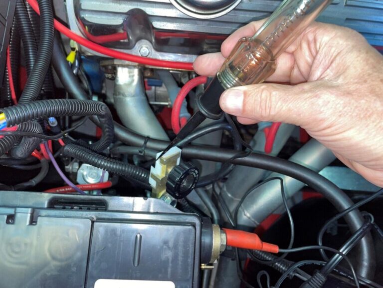 A mechanic using a test light on a battery terminal to test for an electrical short.