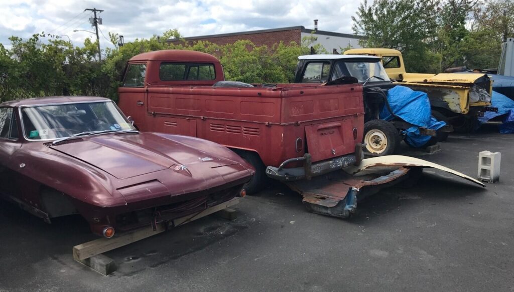 Red Chevy Corvette, red VW van, and 2 Chevy pickup trucks awaiting car restoration outside of a car restoration shop risks